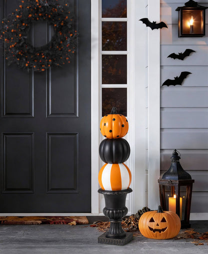 Halloween pumpkin topiary with orange and white striped pumpkin, black pumpkin, and black urn on porch with fall leaves