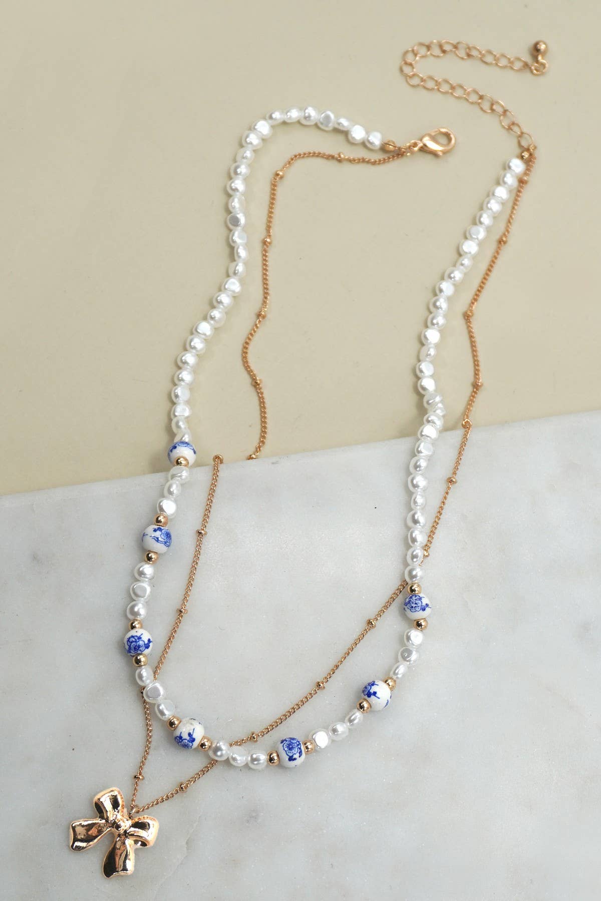 Layered necklace with gold chain with bow charm and white beads with blue toile pattern