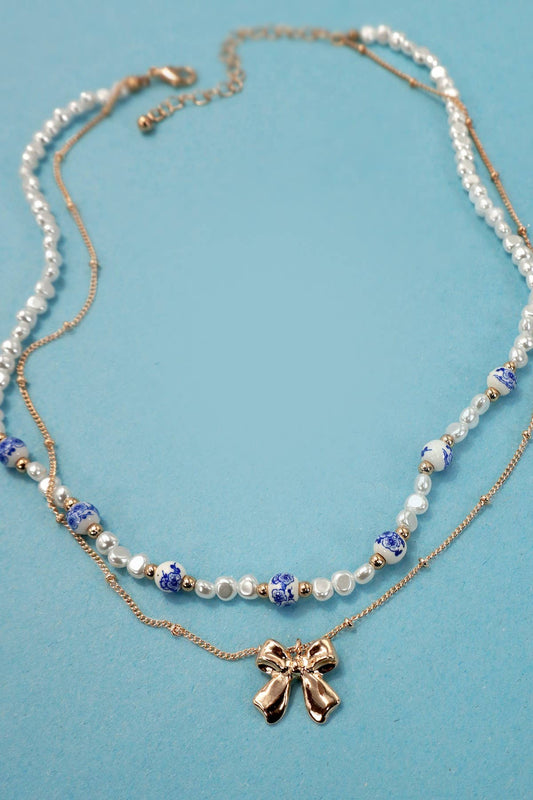 Layered necklace with bow charm and white beads with blue toile pattern