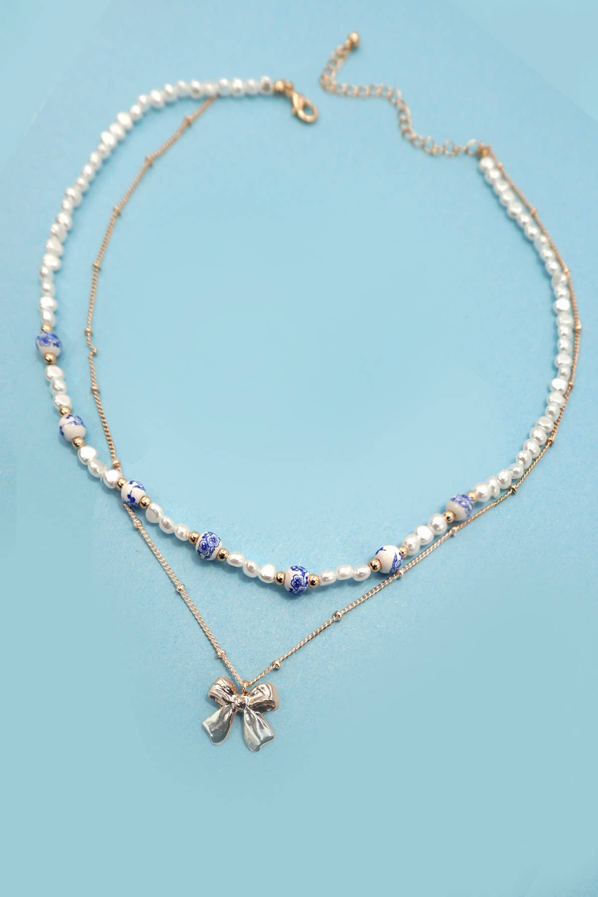 Layered necklace with gold chain with bow charm and white beads with blue toile pattern